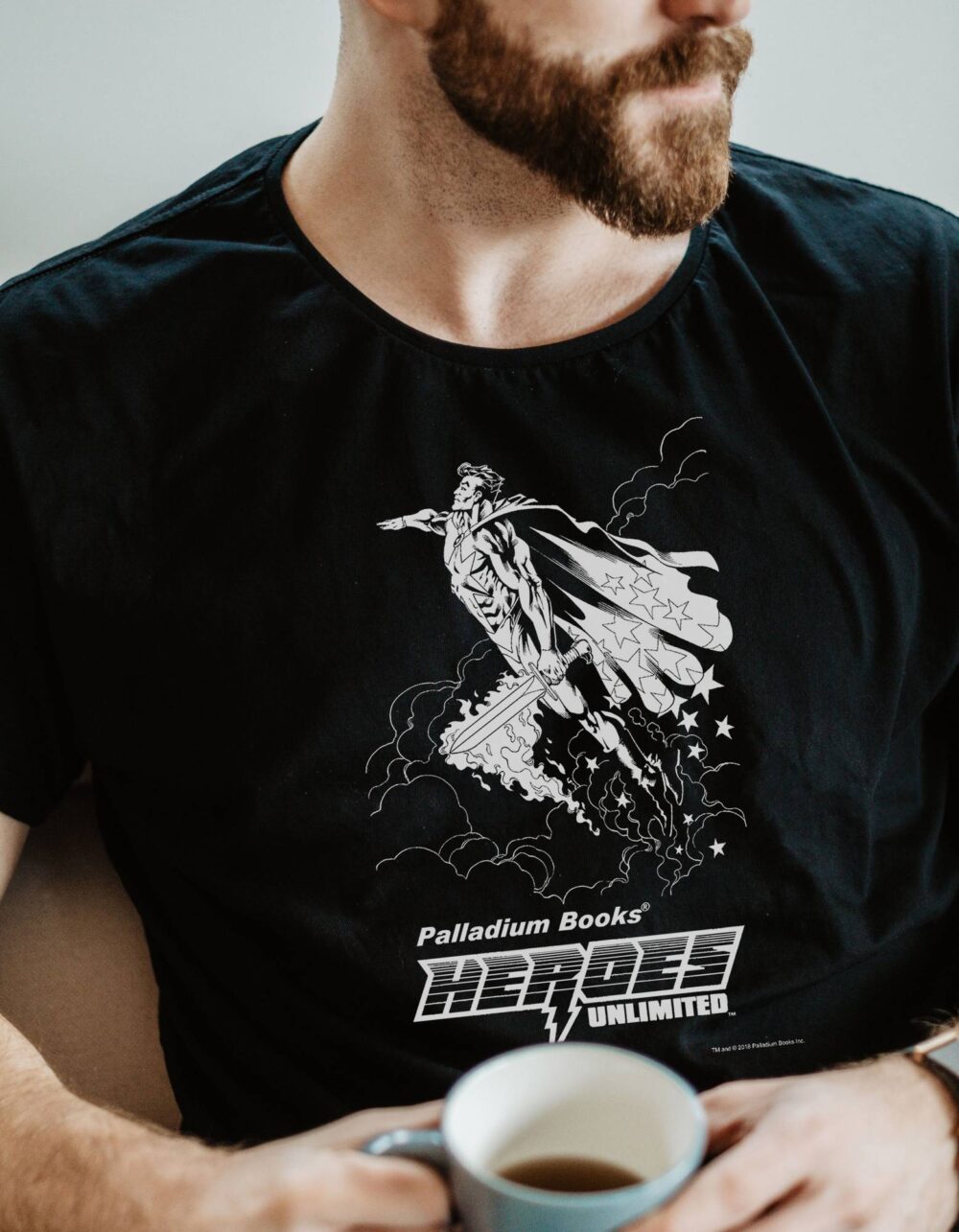 A black shirt with Palladium Books Heroes Unlimited written in white on it and a picture of a super hero flying with a cape and sword